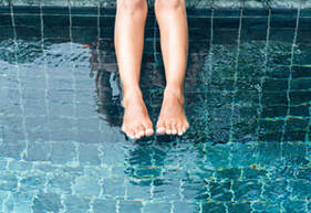 Woman hanging her legs over a green and dark blue tile pool.